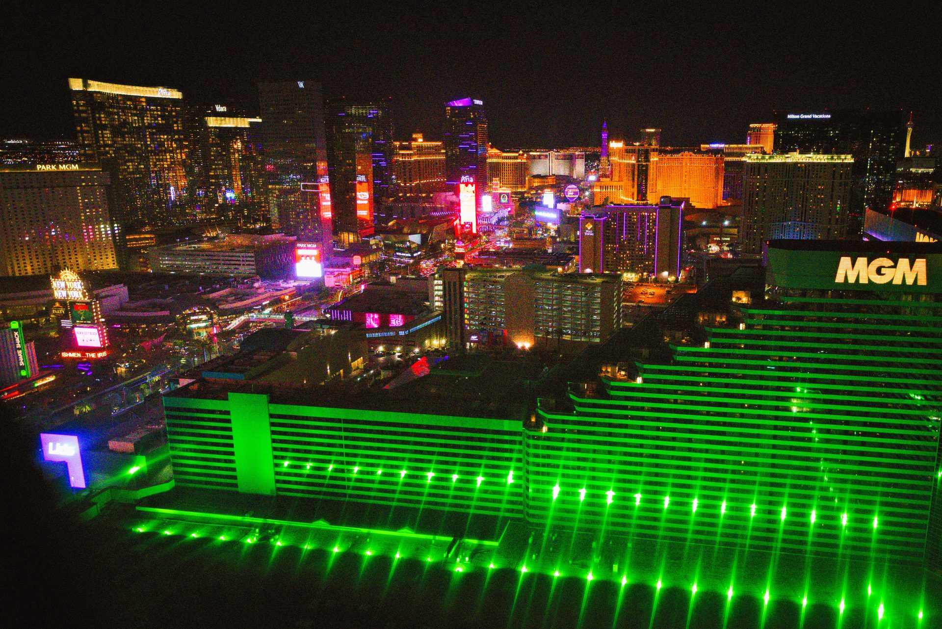 Aerial night view of the Las Vegas Strip skyline lit in green and neon, seen from a helicopter tour